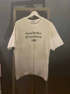 Acne Studios T‑shirt – Stockholm 1996 - Klassisk vit tee från Acne Studios med ikoniskt print framtill. Minimalistisk, clean och lätt att matcha. Har använts ca 4 gånger och är i nyskick.