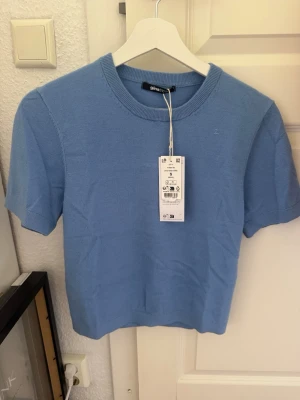 Ljusblå stickad topp Gina Tricot - Supersöt ljusblå stickad topp från Gina Tricot med rund halsringning och korta ärmar. Perfekt till jeans eller kjol för en fräsch look. Mjuk och skön kvalitet som känns lyxig mot huden.
