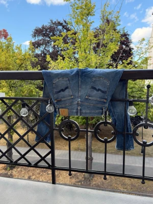 Blå Nudie jeans  - Säljer ett par klassiska blå jeans med smal passform och snygga vågmönster på bakfickorna. Jeansen har normal midja och är gjorda i ett mjukt denimtyg. Perfekta till en avslappnad look och passar till det mesta i garderoben. Storlek W30 L30