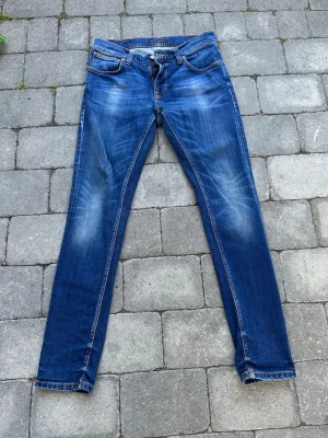 Blå slim fit jeans med slitningar - Säljer ett par blå slim fit jeans med snygga slitningar och tvättade detaljer på låren och knäna. Jeansen har klassisk femficksmodell, normalhög midja och kontrastsömmar. Materialet är denim i bomull med lite stretch för skön passform.