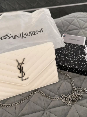 Vit axelremsväska - Säljer en elegant vit med silverfärgad kedja och ikonisk ogga framtill. Väskan har ett quiltat mönster och är tillverkad i läder. Perfekt accessoar för dig som vill ha något stilrent och lyxigt.