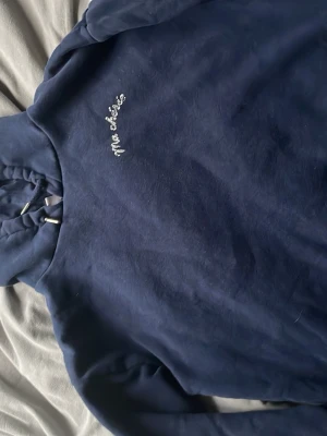 Mörkblå hoodie med text Ma chérie - Mysig mörkblå hoodie med huva och dragsko. På bröstet står det 'Ma chérie' i vit glittrig text. Hoodien har en klassisk passform och är tillverkad i mjukt material, perfekt för en avslappnad stil.