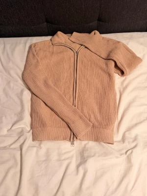 Skön slimfit fullzip cardigan i beige storlek S passar även M - Snygg beige ribbstickad tröja med dragkedja framtill och hög krage. Tröjan har långa ärmar och är tillverkad i ett mjukt, stretchigt material som ger en skön passform. Perfekt för lager på lager och enkel att styla till olika outfits.