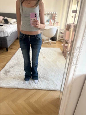 Blå bootcut jeans med låg midja - Säljer ett par blå bootcut jeans med låg midja och klassiska fem fickor. Jeansen har en snygg tvätt med lätt slitning och sitter tajt över låren för att sedan bli vidare nedtill. Perfekta för dig som gillar en retro och avslappnad stil.
