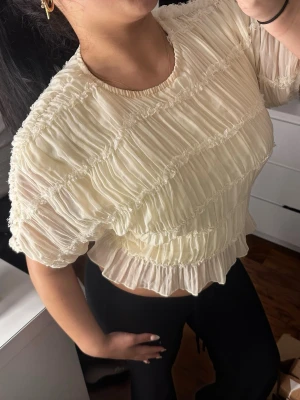 Vit volangig  blus - Säljer en superfin vit blus med volangdetaljer tajt  passform. Toppen har korta ärmar och är gjord i ett lätt, skirt material som ger en luftig känsla. Perfekt för dig som vill ha en söt och trendig topp till sommaren.