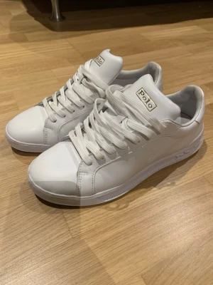 Vita Polo sneakers i läder - Stilrena vita sneakers från Polo med klassisk låg profil och vita skosnören. Skorna är tillverkade i slätt läder och har diskret logga på sidan samt Polo-märke på plösen. Perfekta för dig som gillar en clean och enkel look.