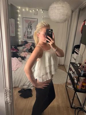 Vit volangig linnetopp - Säljer en superfin vit linnetopp med tunna axelband och flera lager volanger. Toppen är croppad och har en luftig, flowy känsla som passar perfekt till sommaren. Enkel att styla med både jeans och kjol för en trendig look.