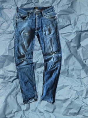 Lee jeans - Säljer ett par blå jeans från Lee W32 L34 i modellen ”Daren Zip Fly” med slitningar på både fram- och baksida. Jeansen har klassiska fem fickor, dragkedja och knapp i midjan samt Lee-lapp bak. Perfekta för en avslappnad och trendig look. Fråga gärna om ni undrar något. Pris är inte hackat i sten.