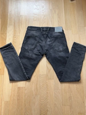 Svarta jeans från Replay - Snygga svarta Anbass jeans från Replay diskreta slitningar. Jeansen har en modern passform och är tillverkade i stretchigt denimtyg för extra komfort. Perfekta för dig som gillar en stilren och trendig look. Inga tecken alls på användning och köpta på NK i Stockholm för nån månad sedan, tveka inte på att höra av dig!