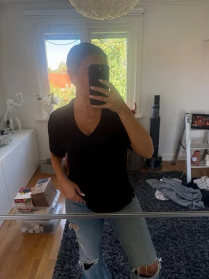 Svart v-ringad topp från Indiska - Svart v-ringad topp från Indiska i mjuk bomull. Toppen har korta ärmar och en avslappnad passform som gör den enkel att styla till olika looks. Perfekt för dig som gillar basic men ändå vill ha något snyggt och bekvämt.