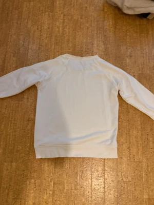 Vit sweatshirt från Gant - Klassisk vit sweatshirt från Gant med rund halsringning och diskret logga på bröstet. Tröjan har långa ärmar och ribbade muddar vid ärmslut och nederkant. Perfekt för en clean och enkel stil. Billigare vid snabba köp