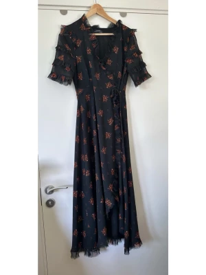 ZARA - Svart blommig omlottklänning - storlek S - Superfin svart omlottklänning från ZARA i storlek S med volanger och blommigt mönster i brunt / orange / rostrött. Snygga korta transparenta ärmar med volangdetaljer och smickrande V-ringning med volang. Nederkanten har också volangdetaljer. Vackert finvävt meshtyg med foder. Smickrande tidlös modell som är lika enkel att styla för fest som för jobb / vardag. Mycket gott skick!