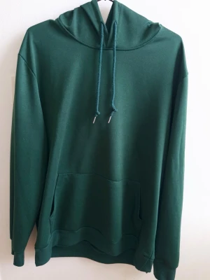 Svart hoodie med ficka - En stilren svart hoodie med huva och dragsnören. Hoodien har en stor magficka framtill och ribbade muddar vid ärmar och nederkant. Tillverkad i mjukt material som känns skönt mot huden. Perfekt för en avslappnad look. Bra och ha för träning 