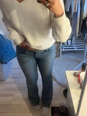 Blå bootcut jeans med låg midja - Säljer ett par klassiska blå bootcut jeans med låg midja och snygga sömdetaljer. Jeansen har en normal passform och är tillverkade i ett mjukt denimtyg som sitter skönt hela dagen. Perfekta till en stickad tröja eller t-shirt.