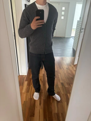 Grå stickad kofta Casual Friday - Mysig grå kofta med v-ringning och knäppning framtill. Tillverkad i mjukt stickat material och har ribbade muddar vid ärmslut och nederkant. Perfekt att slänga över en t-shirt för en enkel och stilren look.