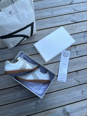 Maison Margiela - Snygga vita sneakers från Maison Margiela | Strl 43 (EU) | Klassiska Replica GAT | Ovandel i premiumläder & mocka | Gummisula i klassisk gum-finish | Stilren & lyxig look | Kvitto från NK + box medföljer | Mycket fint skick | Hör av dig vid minsta fundering!