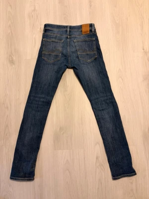 Jack & Jones Jeans  - Säljer ett par blå slim fit jeans från Jack & Jones med klassiska fem fickor. Modellen heter Slim/Glenn. Jeansen har en läderpatch bak i midjan och kontrastsömmar. Perfekta för dig som gillar en avslappnad och trendig look. Storlek: 29/32