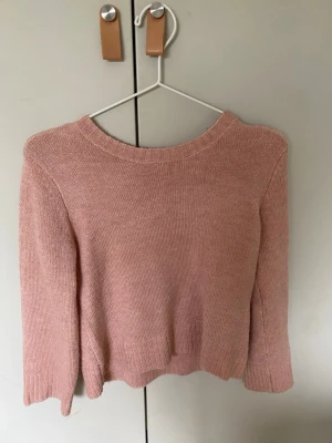 Ljusrosa stickad tröja - Söt ljusrosa stickad tröja med rund halsringning och långa ärmar. Tröjan har en enkel, rak passform och ribbade muddar vid ärmslut och nederkant. Perfekt att matcha med jeans eller kjol för en avslappnad look. Ett väldigt litet hål på baksidan som bara syns om man letar!