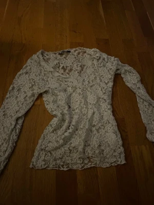 Vit spetsblus med v-ringning - Säljer en superfin vit långärmad blus i spets med v-ringning. Blusen är genombruten med blommigt mönster och har en feminin, figurnära passform. Perfekt att styla med jeans eller kjol för en trendig look. 