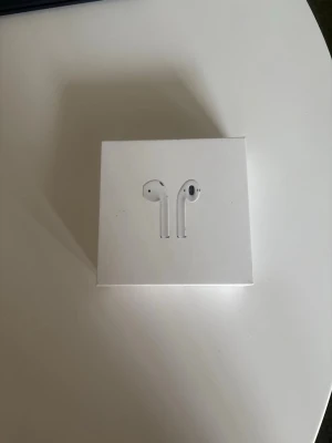 Apple AirPods med laddningsetui - Säljer ett par vita Apple AirPods med laddningsetui. Trådlösa hörlurar i stilren design som funkar smidigt med iPhone, iPad och Mac. Perfekta för musik, samtal och poddar. Levereras i originalförpackning.