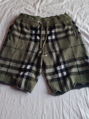 Rutig shorts från Burberry, grön M - Snygga gröna shorts från Burberry med klassiskt rutigt mönster i svart, vitt och beige. Shortsen har snörning i midjan och två fickor på sidorna. Perfekta för en avslappnad och trendig stil.