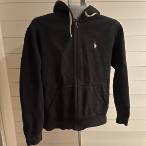 Svart hoodie från Polo Ralph Lauren - Mörkgrå från Polo Ralph Lauren med vit broderad logga på bröstet. Den säljs då den int kommer till användning. Köptes ny för 1900kr
