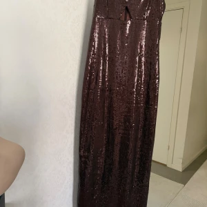 Brun glittrig långklänning med slits - Säljer en helt ny , oanvänd brun glittrig långklänning med tunna axelband och en liten cut-out framtill. Klänningen har figurnära passform, slits baktill och är täckt av paljetter som ger en riktigt snygg partyvibe. Perfekt för dig som vill sticka ut och glänsa. Nypris 599kr