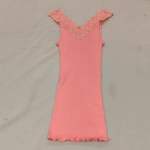 Rosa ribbad linnetopp med spets XL - Supersöt ljusrosa linnetopp från First Class Choice i storlek XL. Toppen har breda axelband med blommig spets och v-ringad hals. Ribbad struktur i mjuk mix av silke och bomull, med vågig kant nedtill. Perfekt för dig som gillar romantiska detaljer. Tyget är stretchigt och kan passa på någon som har storlek M. 