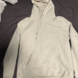  Garde Grisch hoodie - Snygg ljusgrå hoodie från Garde Grisch med broderad GG-logga på bröstet. Passar dig som är 180-187. Tröjan har huva med snörning, magficka och långa ärmar. Mjuk bomullsmix som är perfekt för chill dagar. Enkel och stilren design som funkar till allt.