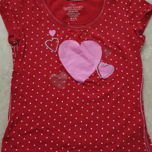 T-shirt - Säljer en röd kortärmad t-shirt från Faded Glory med vita prickar och flera rosa hjärtan framtill. T-shirten har rund hals och är tillverkad i mjuk bomull, perfekt för dig som gillar söta detaljer och färgglada prints.