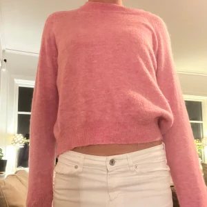 Rosa stickad tröja med rund hals - Mysig rosa stickad tröja med rund hals och långa ärmar. Tröjan har en mjuk och fluffig känsla, ribbade muddar vid ärmslut och nederkant samt en något loose passform. Perfekt för dig som gillar färg och vill ha en chill look.