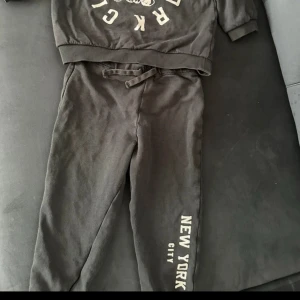 Svart sweatshirt med björntryck - Cool svart sweatshirt med tryck av en söt björn och texten 'New York City' i vitt. Tröjan har ribbade muddar och lång ärm, tillverkad i mjuk bomull. Perfekt för dig som gillar streetstyle och bekväma kläder.storlek 92/barn 