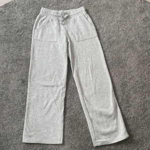 Grå mjukisbyxor från 157, storlek 150 - Snygga ljusgrå mjukisbyxor från 157 med raka ben och bred resår i midjan. Byxorna har snörning och två stora fickor fram, perfekta för chill dagar. Tillverkade i mjukt bomullsmaterial som är superbekvämt.