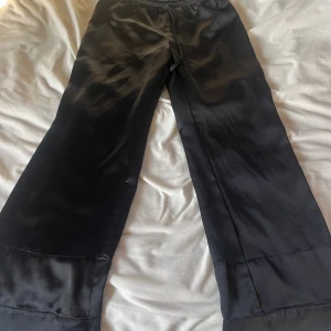 Svarta vida satinbyxor med snörning - Snygga svarta byxor från Zara i glansigt satinmaterial. Modellen är vid med rak passform och har elastisk midja med snörning för extra komfort. Perfekta för dig som gillar en chill och trendig look.