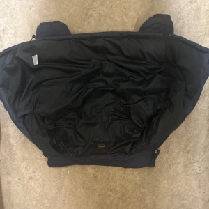 Mörkblå dunjacka från Polo Ralph Lauren - Snygg mörkblå dunjacka från Polo Ralph Lauren med huva och två dragkedjeförsedda fickor. Jackan har det klassiska röda Polo-logot broderat på bröstet och quiltad design. Perfekt för kalla dagar och har en clean, sportig look. passar S/M