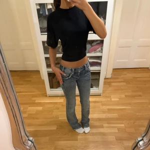 Svart croppad topp från 157, XS - Svart croppad topp från 157 i storlek XS. Modellen har korta, lite bredare ärmar och en rund halsringning. T-shirten är enkel och stilren, perfekt till jeans eller kjol. Materialet känns mjukt och lätt mot huden. Snygg passform som framhäver midjan.