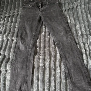 Nudie grå jeans straight fit - Snygga grå jeans från Nudie med klassisk femficksdesign och raka ben. Jeansen har en diskret tvättad look och är tillverkade i mjukt jeanstyg med dragkedja och knappstängning. Passar dig som gillar stilrena och tidlösa jeans.