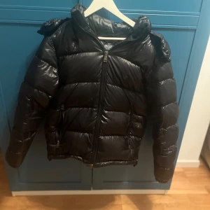 Polo Ralph Lauren The Decker Glossed Down Jacket - Säljer en svart pufferjacka från Polo Ralph Lauren med glansig finish och huva. Jackan har dragkedja framtill, två sidofickor med dragkedja och en schysst, lite puffig look. Perfekt för kalla dagar och riktigt snygg till streetwear-stilen.. original pris ligger runt 5000kr hos mig får du den för mindre än dubbla. Den är S men passar även M som jag sjövl skulle säga jag ligger emellan. Kom privat för qr kod för bevis för att den är äkta