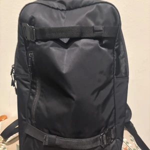 DB skate 18 liter - Snygg svart ryggsäck från Db med stilren design och praktiska spännen framtill. Tillverkad i slitstark polyester med flera fack och vadderad rygg för extra komfort. Perfekt för dig som vill ha en ryggsäck med smarta detaljer och modern look.