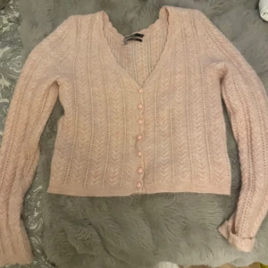 Ljusrosa kofta från Bikbok i ullmix - Superfin ljusrosa kofta från Bikbok i mjuk ullblandning. Koftan har ett snyggt stickat mönster, v-ringad hals och knappar framtill. Långärmad och croppad passform. Aldrig använd!