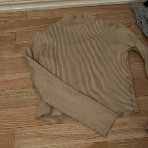 Beige ribbad polotröja från Divided - Säljer en beige ribbad polotröja från Divided by H&M i storlek M. Tröjan har lång ärm och en högre krage som ger en clean och chill vibe. Materialet är mjukt och stretchigt, perfekt för lager på lager under höst och vinter.
