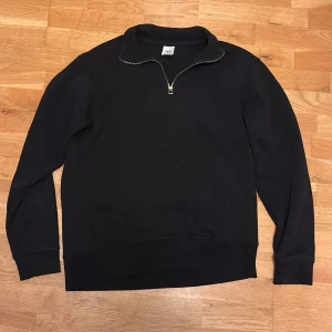 Svart half zip tröja från Zara - Svart långärmad tröja från Zara med halv dragkedja vid halsen. Tröjan har en klassisk, enkel design och är tillverkad i mjukt material som passar perfekt till lager-på-lager. Perfekt för dig som gillar stilrena plagg.