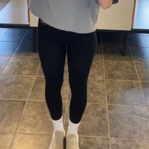 Svarta tränings leggings från MOA - Säljer ett par svarta tränings leggings från MOA med hög midja och tight passform. De är tillverkade i ett stretchigt syntetmaterial som sitter skönt och följer kroppen. Perfekta för träning eller chill. Diskret logga i midjan.