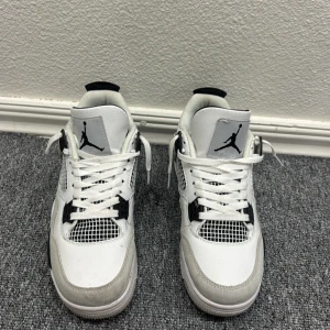 Jordan 4 Millitary Black - Säljer ett par Nike Air Jordan 4 i vit och svart. Skorna har klassisk meshpanel, snörning och Jumpman-logga på plösen och hälen. Ovandelen är i skinn med detaljer i syntet och mesh. Perfekta för dig som gillar streetwear och ikoniska sneakers.