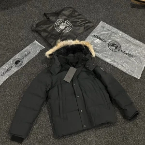 Svart dunjacka med päls från Canada Goose - Säljer en svart dunjacka från Canada Goose med snygg päls på huvan och klassisk logga på ärmen. Jackan har dragkedja och knappar framtill, samt flera praktiska fickor. Perfekt för kalla vinterdagar och har en riktigt schysst look.