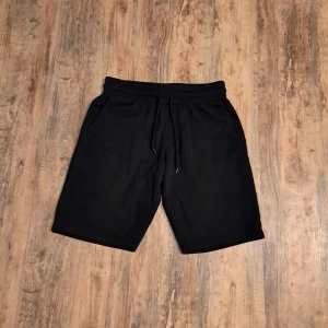 Svarta sweatshorts med snörning - Svarta sweatshorts med elastisk midja och snörning framtill. Modellen har två sidofickor och en bakficka. Perfekta för chill dagar eller träning, tillverkade i mjukt material för maximal komfort.