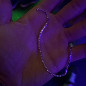 Glittrigt silverarmband med stenar - Snyggt och glittrigt armband i silverfärg med små fyrkantiga stenar längs hela bandet. Perfekt för dig som gillar att sticka ut med lite extra bling. Armbandet är smalt och flexibelt, vilket gör det enkelt att bära och matcha med andra smycken.