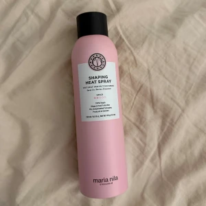 Maria Nila Shaping Heat Spray 250ml - Snygg rosa värmeskyddsspray från Maria Nila, perfekt för styling med värmeverktyg. Flaskan är cylinderformad med svart lock och rymmer 250 ml. Produkten är vegansk och tillverkad i Sverige, med fokus på hållbarhet och värmeskydd för håret.