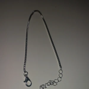 Silvrigt kedjearmband med lås - Stilrent armband i silverfärgad metall med fyrkantiga länkar och ett klassiskt karbinlås. Kedjan har en enkel och modern design som passar till många olika stilar. Perfekt för dig som gillar minimalistiska smycken.