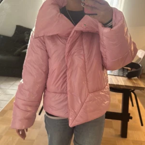 Rosa pufferjacka  - Glansig rosa pufferjacka från Junkyard storlek S, med oversized krage som går att ha upp eller nerfälld, breda ärmar, knappar framtill och två stora fickor på sidorna. Perfekta jackan i vinter. Använd ett par gånger. Om du har funderingar inför ditt köp är det bara att skriva till mig!